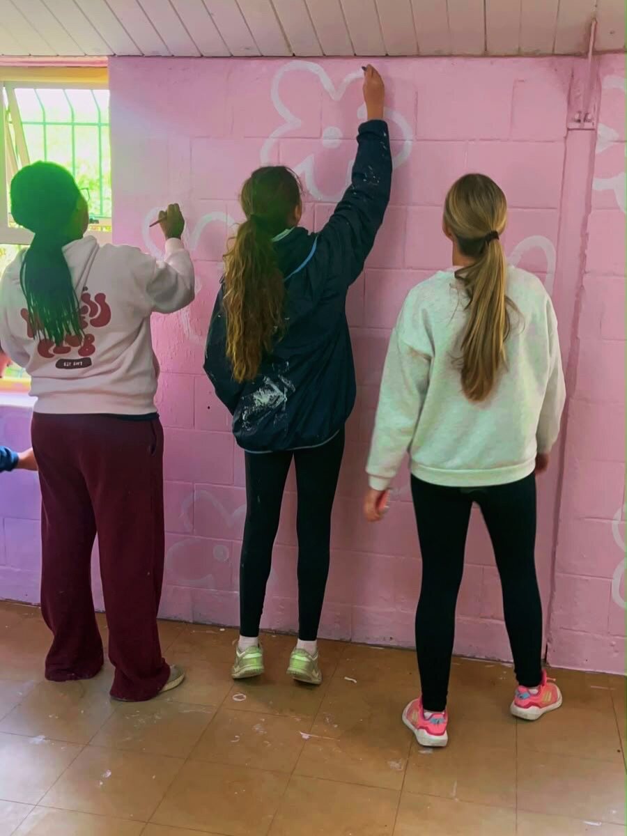 Volunteers painting flowers on a classroom wall
