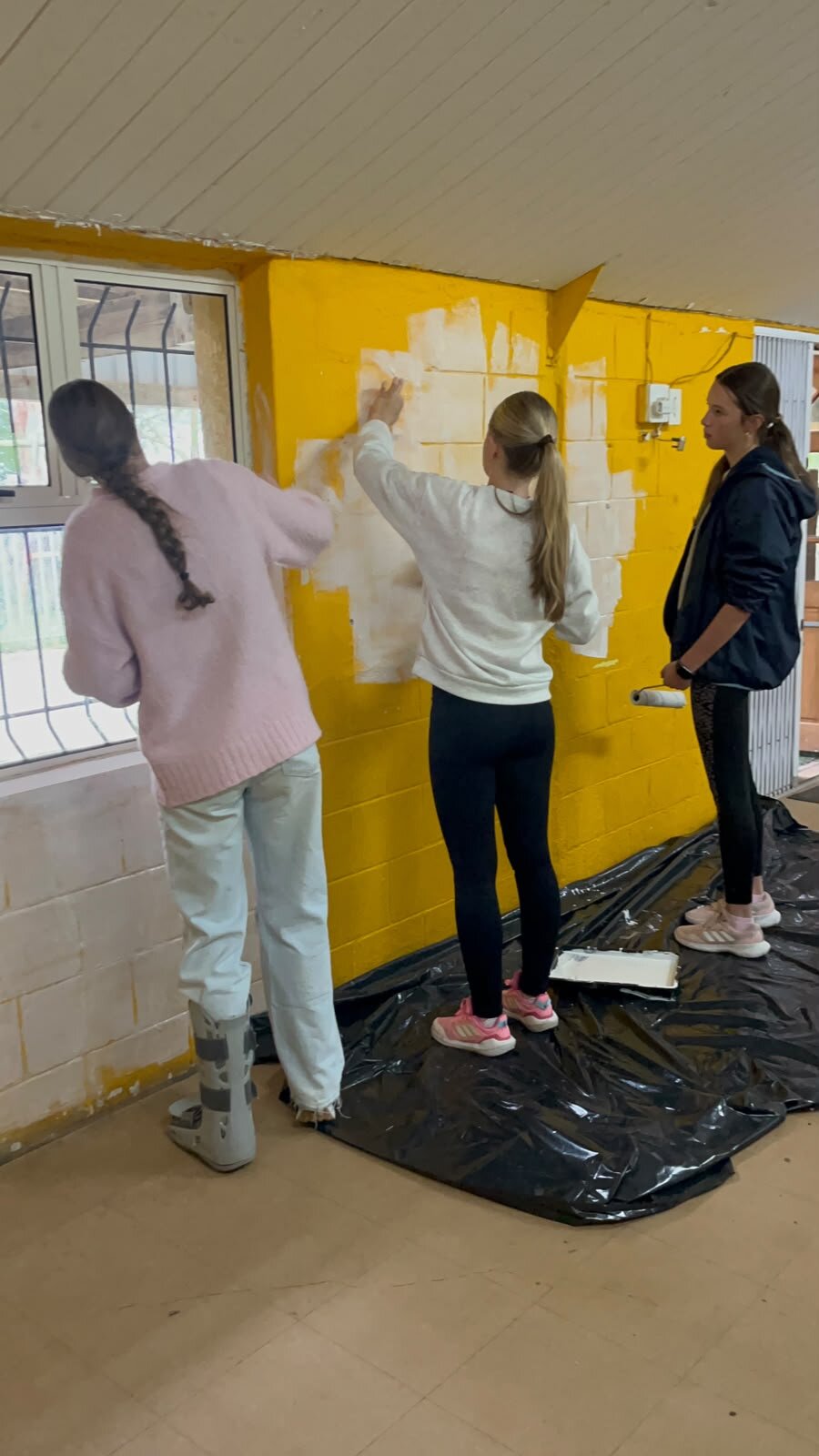 Volunteers painting a yellow wall at Kleenvrygeestes School